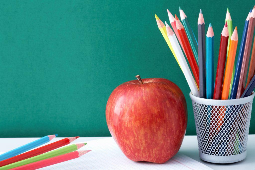 Image of crayons and red apple against blackboard